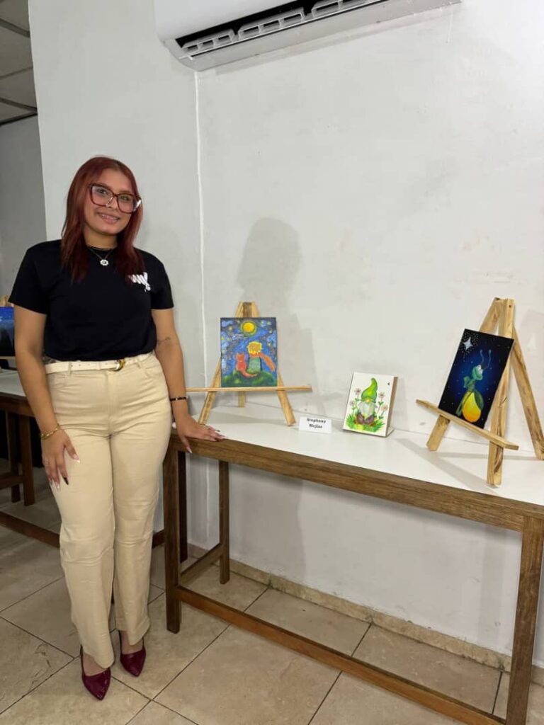 Stephany Mej&iacute;as posa junto a tres obras pict&oacute;ricas durante la exhibici&oacute;n