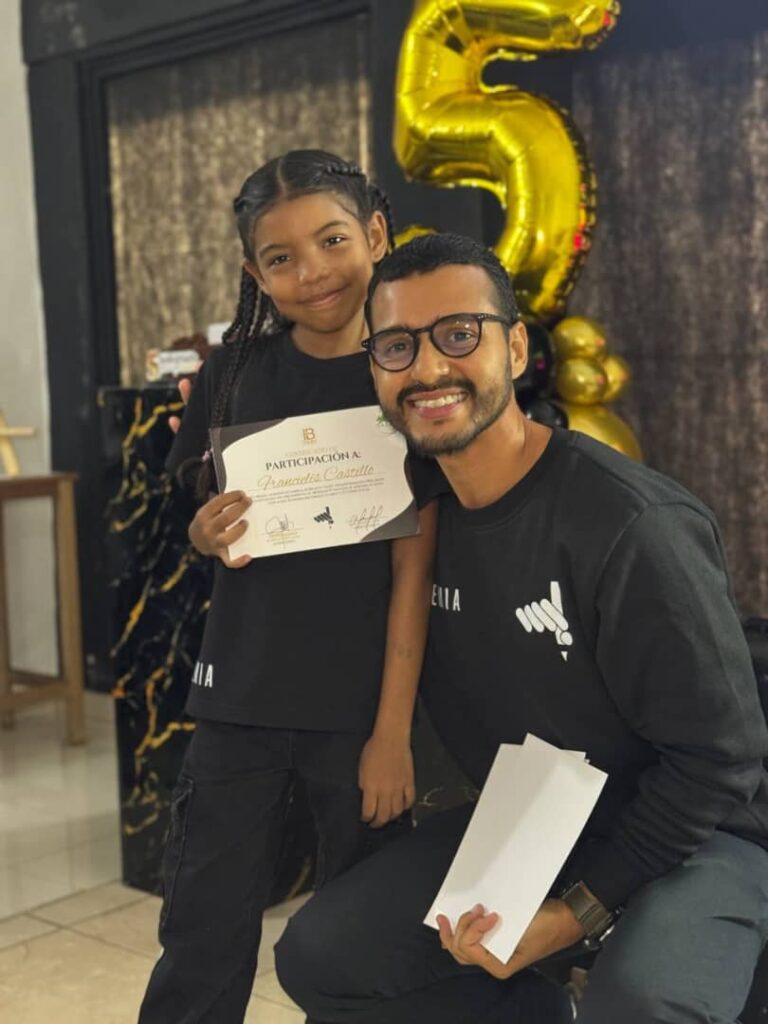 Francielis Castillo posa junto a su profesor mientras muestra un certificado de participaci&oacute;n