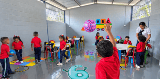 Niños de preescolar participan en actividades dentro de un aula escolar junto a una docente.
