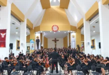 Orquesta y coro juveniles interpretan una obra musical bajo la dirección de un maestro en un recinto religioso.