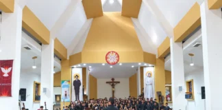 Orquesta y coro juveniles interpretan una obra musical bajo la dirección de un maestro en un recinto religioso.